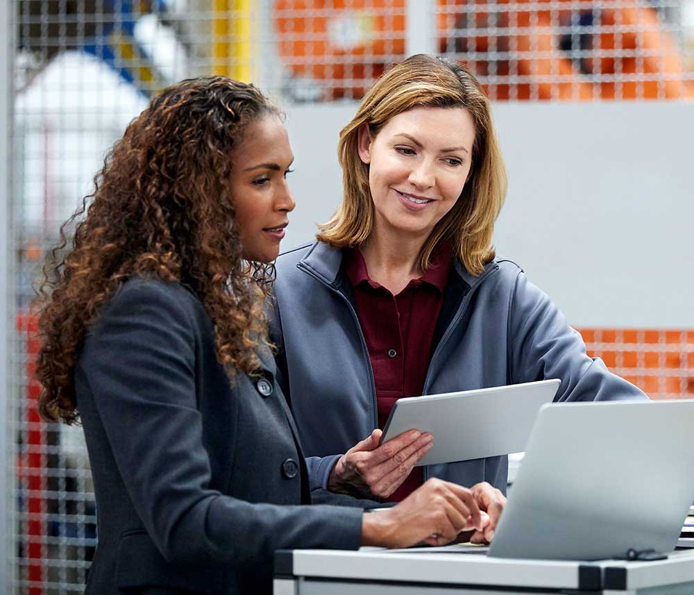 Two women standing in a factory reviewing information on a tablet